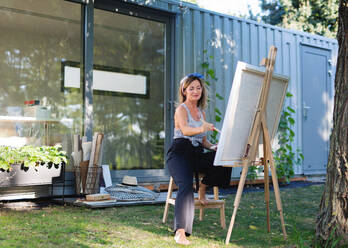 Porträt einer glücklichen reifen Frau mit Palette beim Malen im Freien im Garten. - HPIF15205
