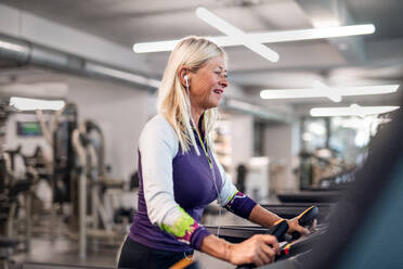 Eine glückliche ältere Frau mit Kopfhörern im Fitnessstudio beim Cardio-Workout-Training. - HPIF15213