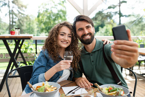 Ein fröhliches Paar hält einen Moment auf einer Restaurantterrasse fest und posiert für ein Selfie mit seinem Smartphone - HPIF15238