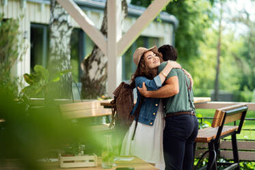 Happy young couple greeting outdoors on terrace restaurant, hugging. - HPIF15239