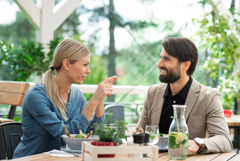 Ein glückliches Paar sitzt an einem Tisch im Freien auf einer Restaurantterrasse und unterhält sich. - HPIF15240