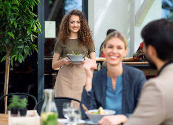 Woman waitress with face mask serving happy couple outdoors on terrace restaurant. - HPIF15241