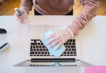 Mittelteil eines nicht erkennbaren jungen Studenten mit Handschuhen am Tisch, der einen Laptop desinfiziert. - HPIF15298