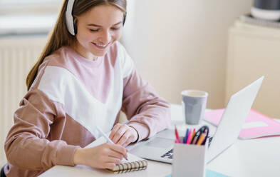 Young happy college female student sitting at the table at home, using laptop and headphones when studying. - HPIF15303