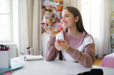 Junge Studentin mit Smartphone am Tisch sitzend, Konzept des Online-Unterrichts. - HPIF15306