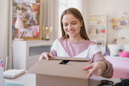 Front view of young female student at the table, opening parcel box. - HPIF15310