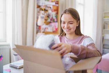 Vorderansicht einer jungen Studentin am Tisch, die einen Paketkasten öffnet. - HPIF15311