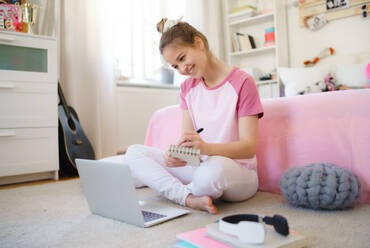 Front view of young girl with laptop sitting on floor, learning during quarantine. - HPIF15323