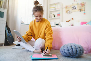 Young girl with tablet sitting and writing on floor, studying during quarantine. - HPIF15327