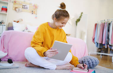 Junges Mädchen mit Tablet auf dem Boden sitzend und schreibend, studiert während der Quarantäne. - HPIF15328