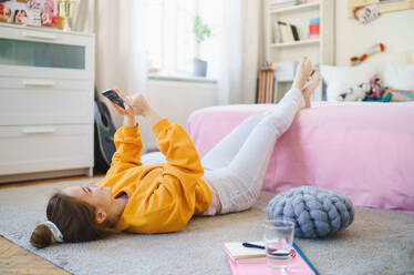 Glückliches junges Mädchen mit Smartphone auf dem Boden zu Hause, das einen Videoanruf tätigt. - HPIF15332