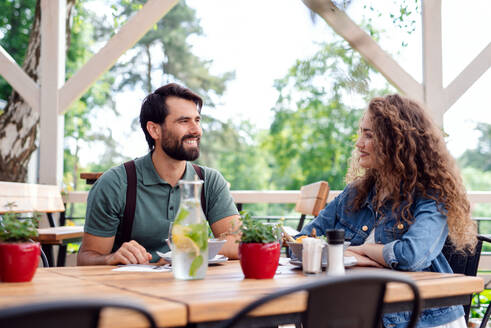 Ein glückliches Paar sitzt an einem Tisch im Freien auf einer Restaurantterrasse und unterhält sich. - HPIF15337