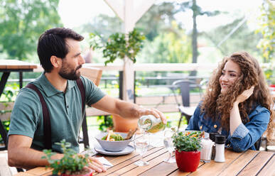 Ein glückliches Paar sitzt an einem Tisch im Freien auf einer Restaurantterrasse und unterhält sich. - HPIF15339