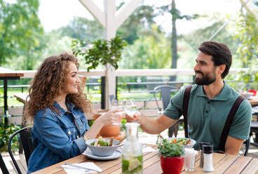 Glückliches junges Paar sitzt im Freien auf einer Restaurantterrasse und stößt mit Gläsern an. - HPIF15341