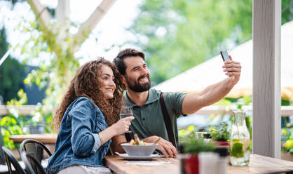 Happy couple sitting outdoors on terrace restaurant, taking selfie with smartphone. - HPIF15344