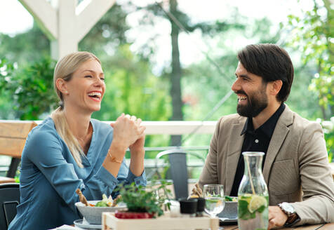 Ein glückliches Paar sitzt an einem Tisch im Freien auf einer Restaurantterrasse und unterhält sich. - HPIF15351