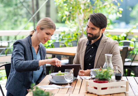 Glückliches Paar sitzt am Tisch im Freien auf der Terrasse eines Restaurants und isst. - HPIF15354