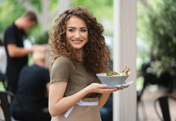 Portrait of waitress with plate standing on terrace restaurant, looking at camera. - HPIF15359