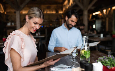 Glückliches junges Paar sitzt in einem Restaurant und betrachtet die Speisekarte. - HPIF15365