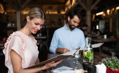 Happy young couple sitting indoors in restaurant, looking at menu. - HPIF15365