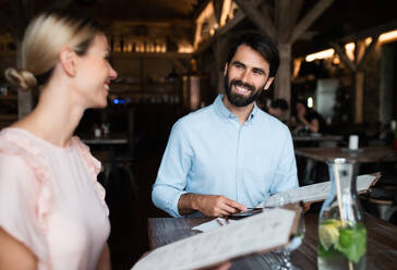 Ein glückliches Paar sitzt drinnen in einem Restaurant, schaut auf die Speisekarte und unterhält sich. - HPIF15366