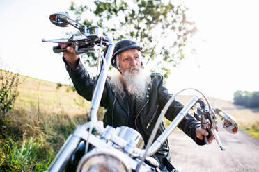 Ein älterer Mann, der mit seinem Motorrad auf dem Lande unterwegs ist und sich ausruht. - HPIF15374