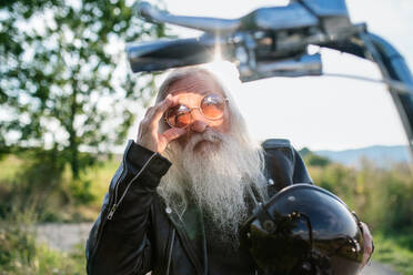 Ein älterer Mann mit Motorrad und Sonnenbrille auf dem Lande. - HPIF15386