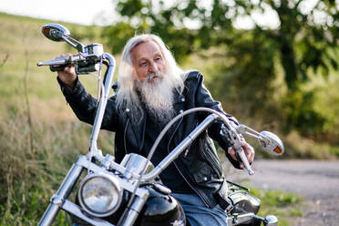 Ein älterer Mann, der mit seinem Motorrad auf dem Lande unterwegs ist und sich ausruht. - HPIF15397