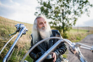 Ein älterer Mann, der mit seinem Motorrad auf dem Lande unterwegs ist und sich ausruht. - HPIF15399