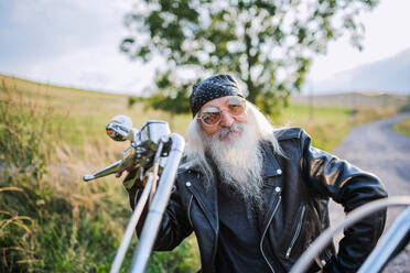Ein älterer Mann mit Motorrad und Sonnenbrille auf dem Lande. - HPIF15401