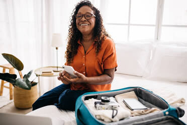 Eine Frau sitzt in ihrem Hotelzimmer und nutzt eine Reise-App, um sich über örtliche Sehenswürdigkeiten zu informieren und ihre Tagesroute zu planen. - JLPSF30374