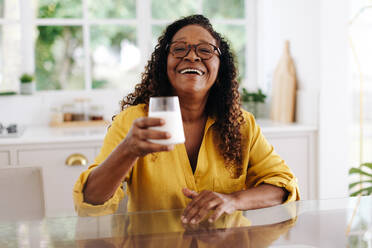 Glückliche Seniorin, die frische Milch trinkt, um Kalzium und andere Nährstoffe zu sich zu nehmen, die die Knochengesundheit und das allgemeine Wohlbefinden fördern. Ältere schwarze Frau, die zu Hause ein Milchprodukt zu ihrer Ernährung hinzufügt. - JLPSF30387