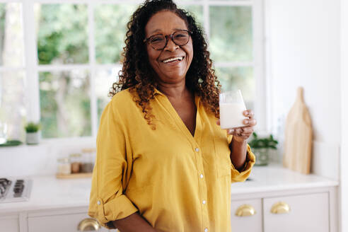 Porträt einer lächelnden Seniorin, die zu Hause ein Glas frische Milch trinkt. Die Frau genießt ihren täglichen Milchkonsum und weiß, dass sie mit jedem Schluck etwas für ihre Gesundheit tut. - JLPSF30388