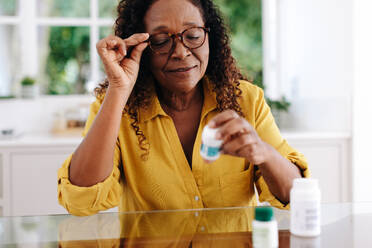 Eine Frau, die das Etikett ihrer verschreibungspflichtigen Medikamente liest, während sie ihre Behandlungsroutine zu Hause einhält. Eine ältere Frau, die proaktive Schritte unternimmt, um ihre chronische Krankheit zu bewältigen und ihre Gesundheit zu erhalten. - JLPSF30402