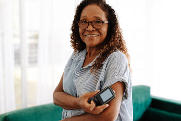 Portrait of a woman using continuous glucose monitoring to manage her diabetes at home. Mature woman using the latest health technology to measure and keep her blood glucose levels under control. - JLPSF30403