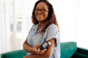 Diabetic woman using a flash glucose monitor to measure her blood sugar levels with a simple scan, allowing her to adjust her diet and medication as needed for optimal health and wellness. - JLPSF30404