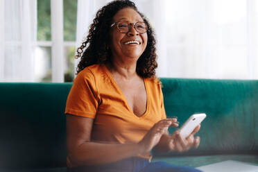 Retired woman using her smartphone to stay connected with her loved ones. Senior woman using mobile technology to make phone calls, send text messages, access social media, and browse the internet. - JLPSF30410