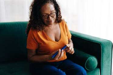 Woman with type 1 diabetes manages her condition by injecting herself with a dose of insulin. Senior woman using a smart health device to regulate her blood sugar levels and maintain a healthy life. - JLPSF30416