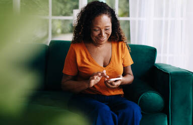 Eine glückliche ältere schwarze Frau, die eine mobile App nutzt, um ihren Lebensstil zu Hause zu verwalten und zu planen, und die die Vorteile der Technologie nutzt, um in ihren goldenen Jahren organisiert und informiert zu bleiben. - JLPSF30426