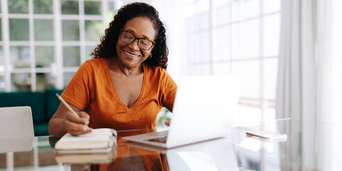 Eine glückliche ältere Frau, die an einem Tisch in ihrem Arbeitszimmer sitzt, ihren letzten Willen in einem Tagebuch niederschreibt und darauf achtet, ihr Vermögen aufzuteilen. Eine Frau im Ruhestand, die einen Plan für die Zukunft aufstellt. - JLPSF30437