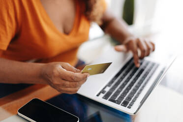 Woman using her gold credit card to make an online payment with a laptop, enjoying the rewards of being a loyal customer. Black female retiree making smart banking choices and maximizing her benefits. - JLPSF30449