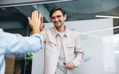 Ein Geschäftsmann feiert einen Teamerfolg, indem er seinem Kollegen in einer Sitzung gratuliert. Ein glücklicher Geschäftsmann beglückwünscht sein Team und motiviert es, weitere Erfolge zu erzielen. - JLPPF01831