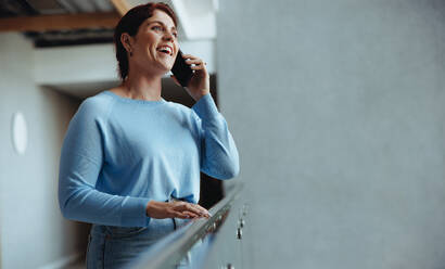 Professional businesswoman happily answering a phone call in an office. Happy caucasian female using a mobile phone to communicate with business partners and associates on behalf of her company. - JLPPF01840