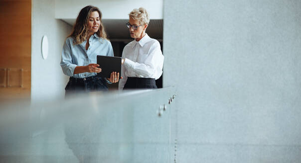 Eine Verwaltungsassistentin zeigt ihrem Chef auf einem digitalen Tablet die Termine, die für sie vorgesehen sind. Eine junge Geschäftsfrau arbeitet mit einer reifen weiblichen Führungskraft an einem modernen Arbeitsplatz. - JLPPF01846