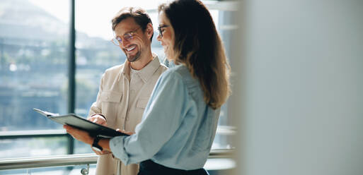 Business professionals going though a report document together in an office. Two business colleagues smiling as they read on the growth and success of their company. - JLPPF01856