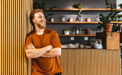 Geschäftsmann, der mit einem glücklichen Lächeln wegschaut, während er vor einem Café in einem modernen Coworking-Büro steht. Erfolgreicher Geschäftsmann, der eine erfrischende Pause in einem Café macht. - JLPPF01861