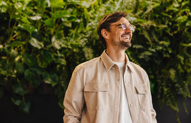 Business man smiles happily as he stands in an eco friendly work environment. Professional man looking proud to be working in an organisation that promotes sustainable values. - JLPPF01862