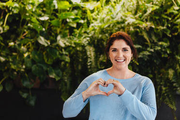 Portrait of a business woman showing a her gesture while standing in an environmentally friendly office. Happy business woman supporting and promoting office sustainability. - JLPPF01866