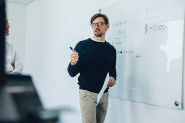 Professional project manager having a discussion with his team as they brainstorm ideas and solutions in a business meeting. Business man leading his colleagues in a financial project. - JLPPF01870