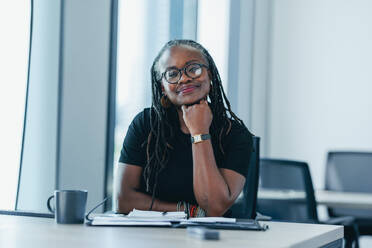 Empowered black business woman looking at the camera with confidence while sitting at her desk. Mature professional expressing self-assurance in her expertise and abilities in a business office. - JLPPF01883